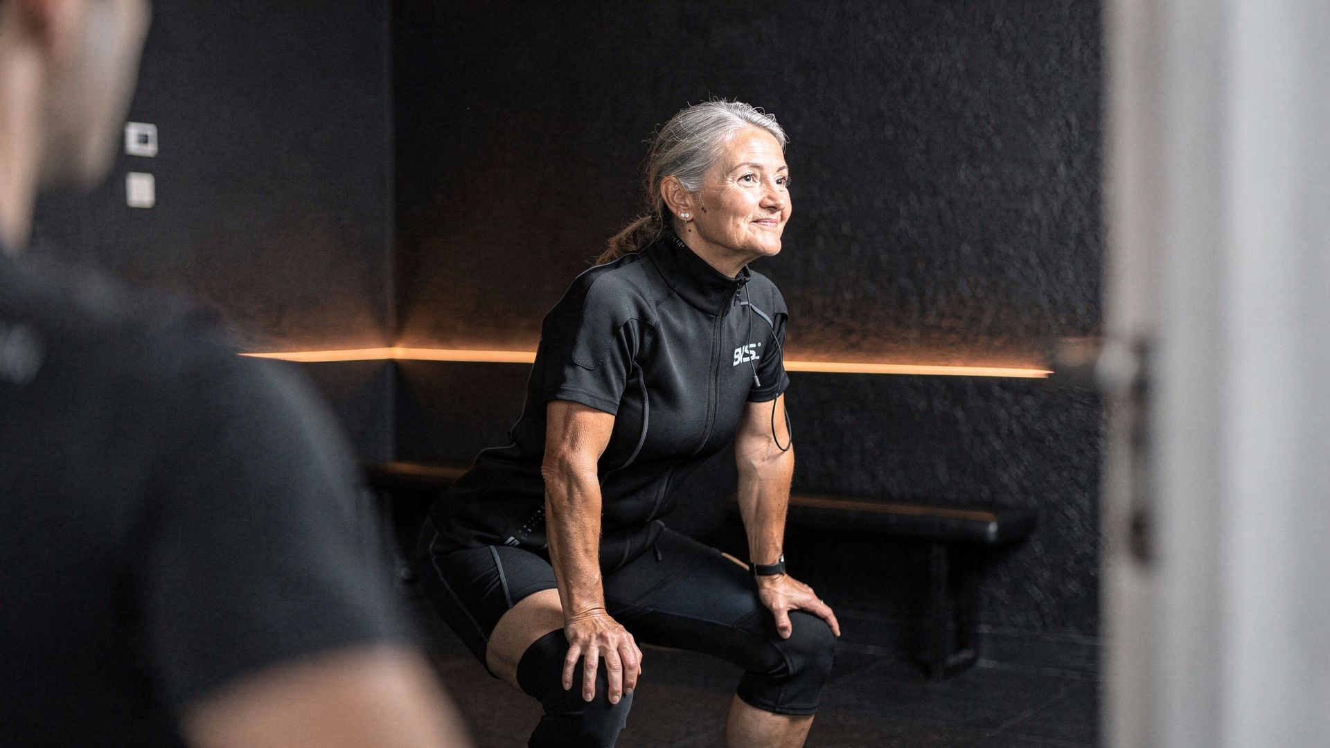 A trainer level with a member mid-squat, one hand steadying her shoulder