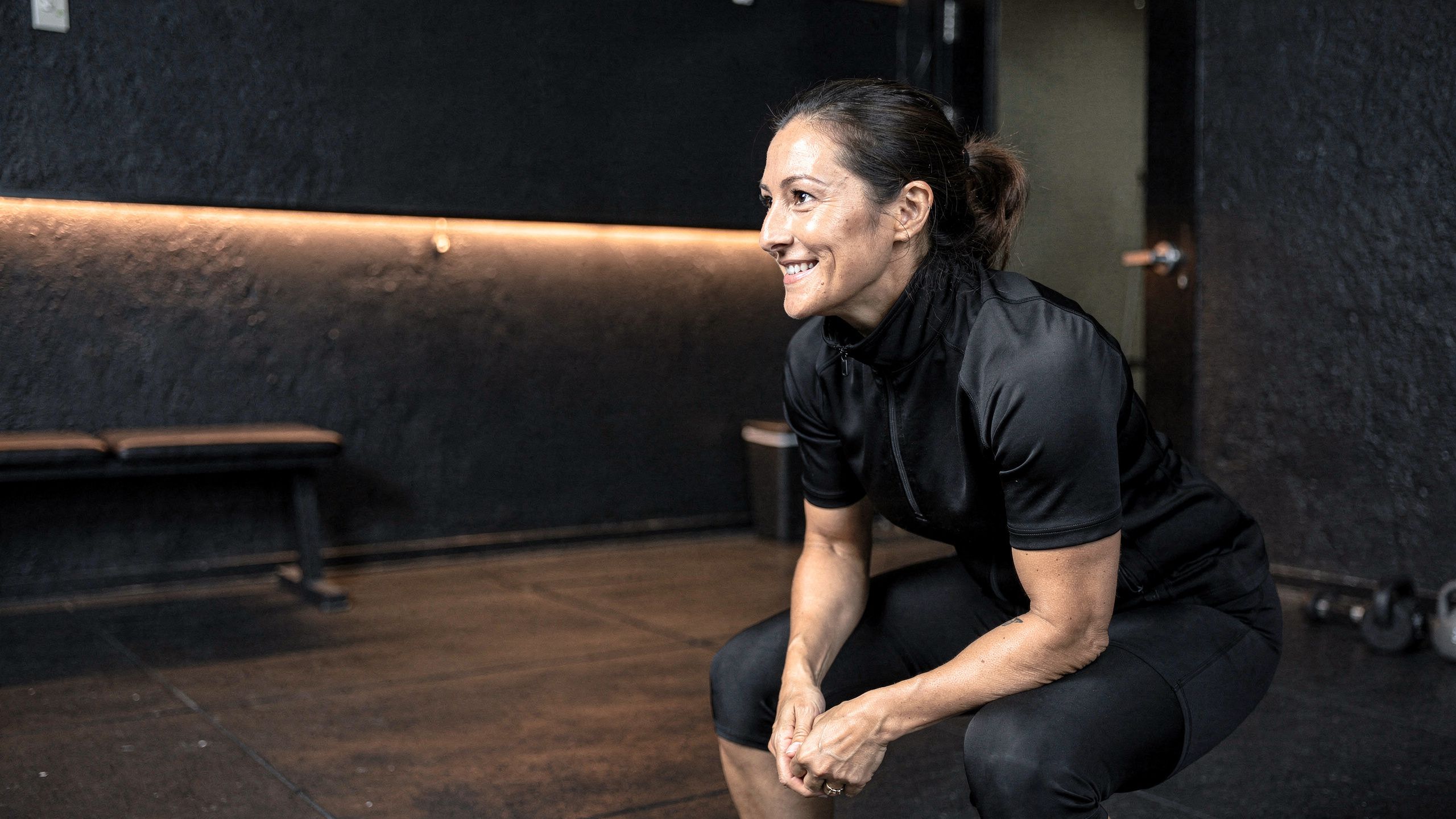 A member holding a slow squat in her training suit, laughing